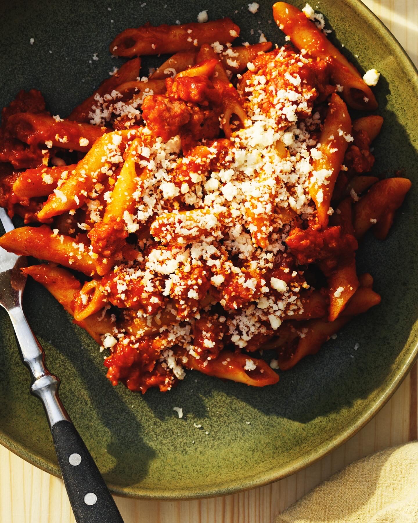 Penne in tomato sauce with grated cheese in a green bowl
